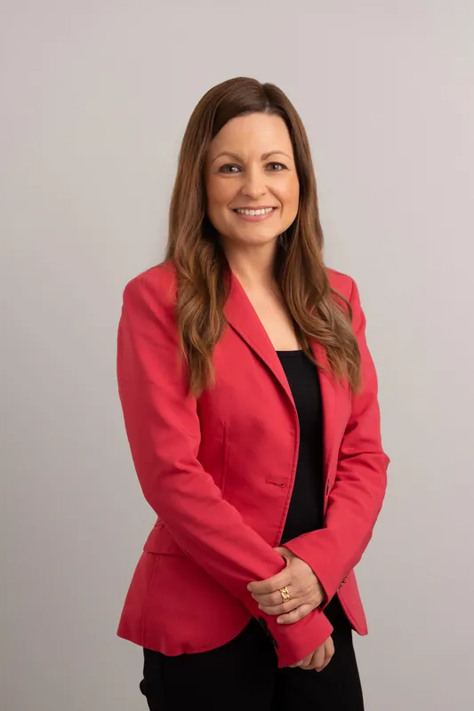 Woman smiling at camera wearing a bright pink blazer over a black top in a studio setting.