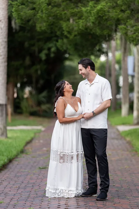 Christian and Dana stand close together on a brick pathway lined with palm trees in dappled sunlight.