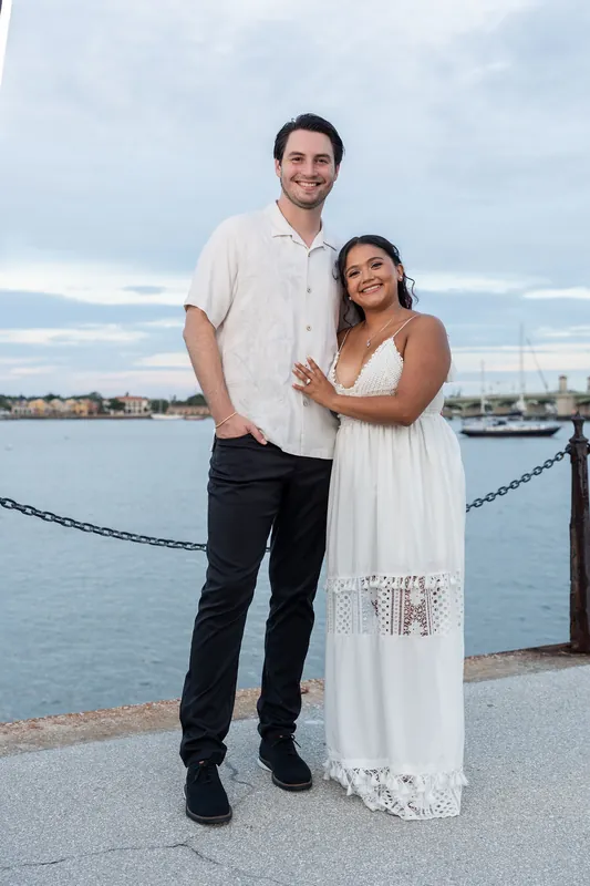 Christian and Dana stand by the waterfront with a rope railing and calm harbor behind them in Downtown St. Augustine.