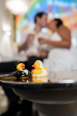 Yellow rubber ducks float in a black bowl at The Tipsy Duck Parlor while Dana and Christian embrace in soft focus behind
