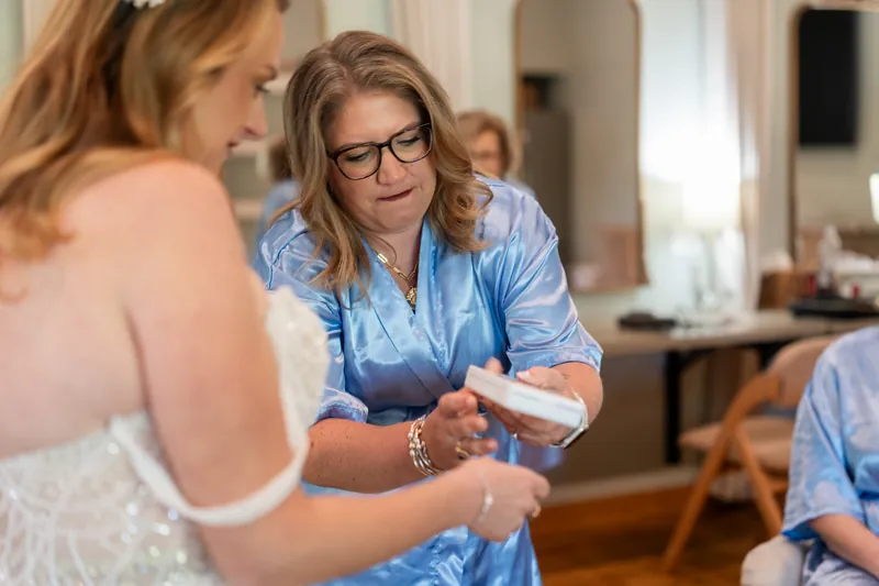Woman in blue shirt helps Danielle with her wedding dress straps before ceremony.