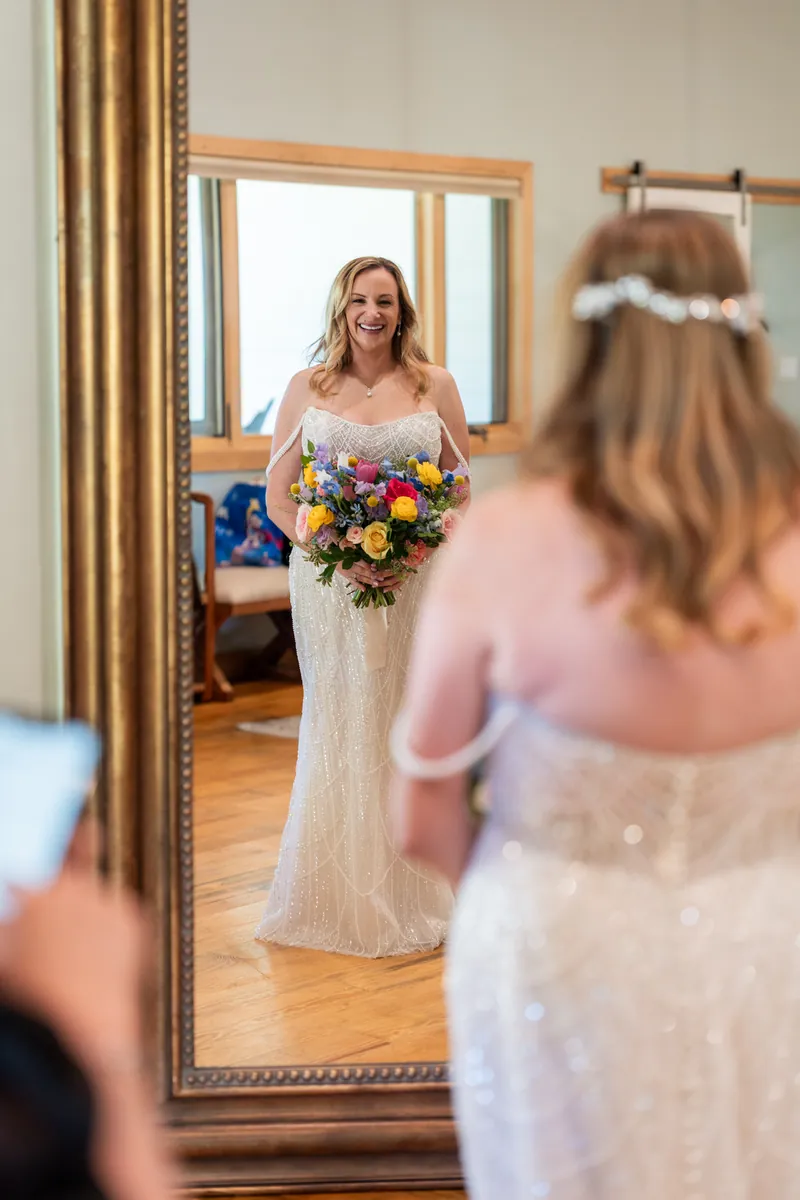 Danielle admires herself in a mirror wearing her beaded white gown and colorful bridal bouquet.