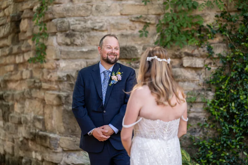 Von and Danielle face each other laughing against an ivy-covered stone wall during their ceremony.