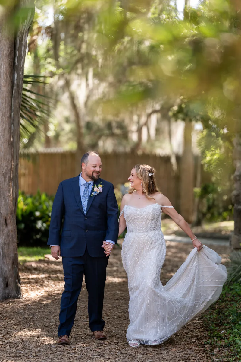 Von and Danielle walk down a tree-lined path with Danielle's veil flowing behind her in the breeze.
