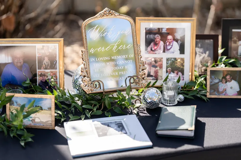 Memorial display with framed photos, greenery, and personalized signs on a black table.
