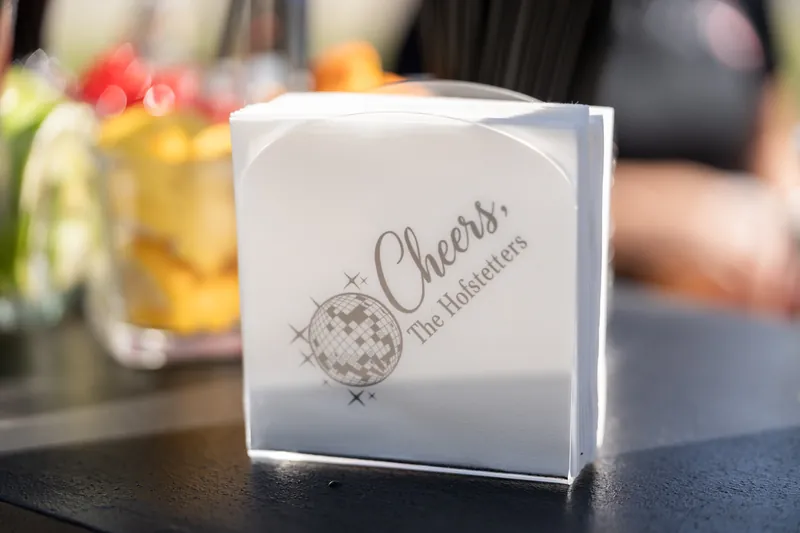 White favor box printed with "Cheers to the Newlyweds" on a reception table.
