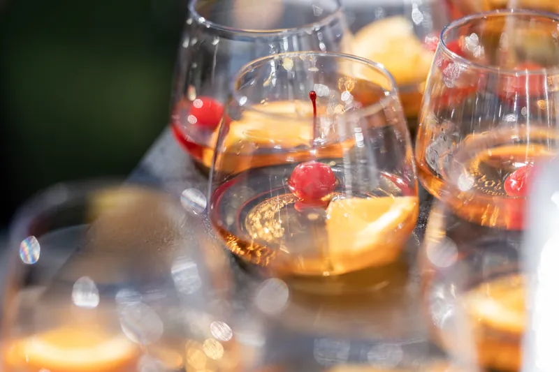 Whiskey cocktails with orange and cherry garnishes lined up on a table.