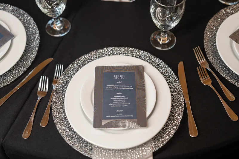 Two place settings with white plates on sparkly charcoal runners, navy menus, and gold flatware.