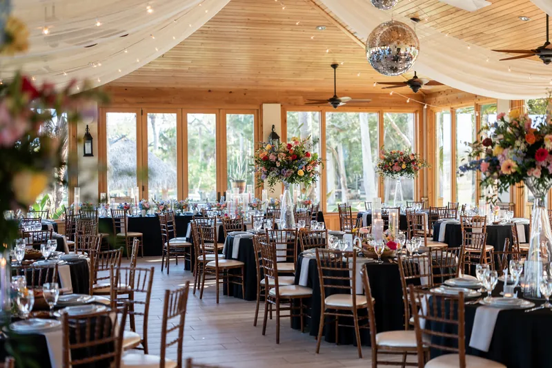 Bright reception space with exposed wood beams, hanging crystals, and abundant floral arrangements in coral and yellow tones.