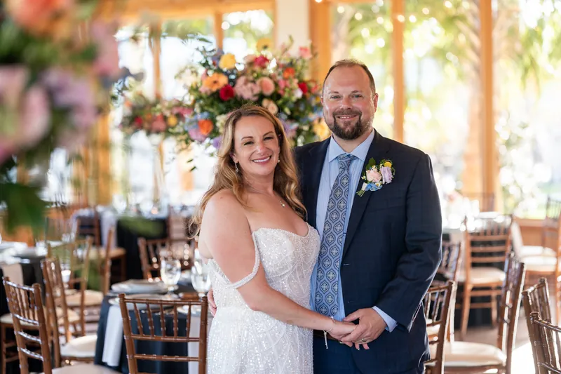 Danielle and Von pose together holding hands in front of coral and yellow floral arrangement in the reception space.