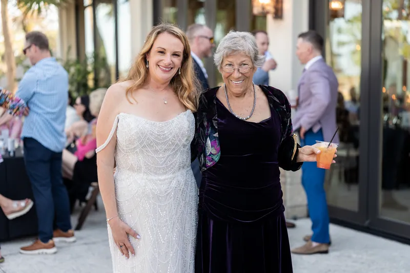 Danielle in wedding dress smiles with an older woman in black velvet dress at the entrance of the wooden venue.