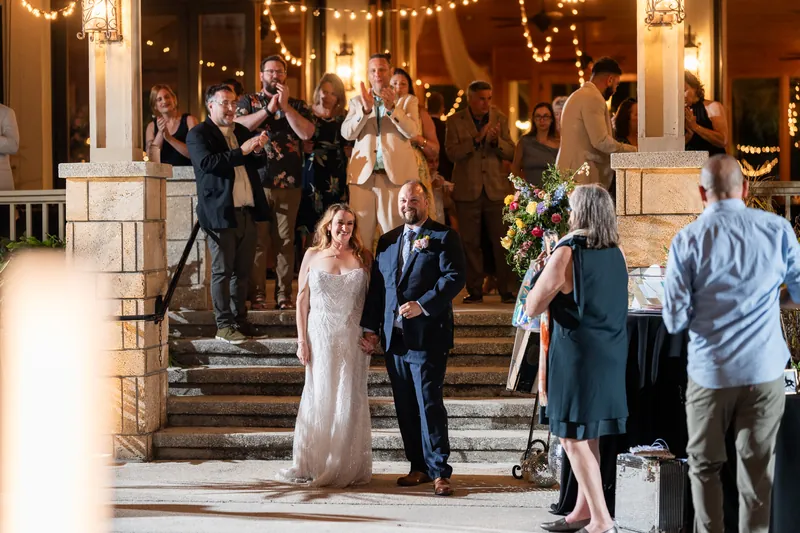 Danielle & Von walking down lit venue steps as guests applaud during evening reception exit.
