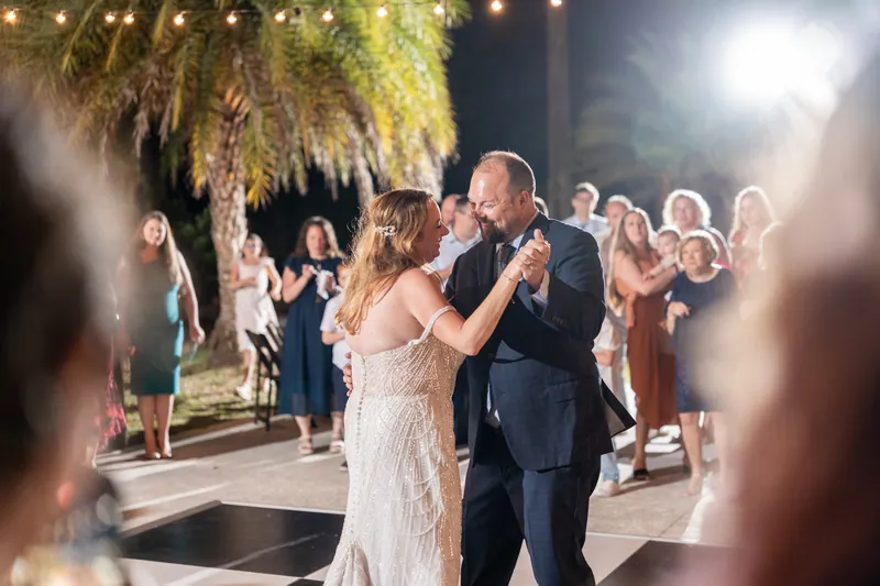 Danielle & Von dancing under string lights and palm fronds as guests watch during reception.