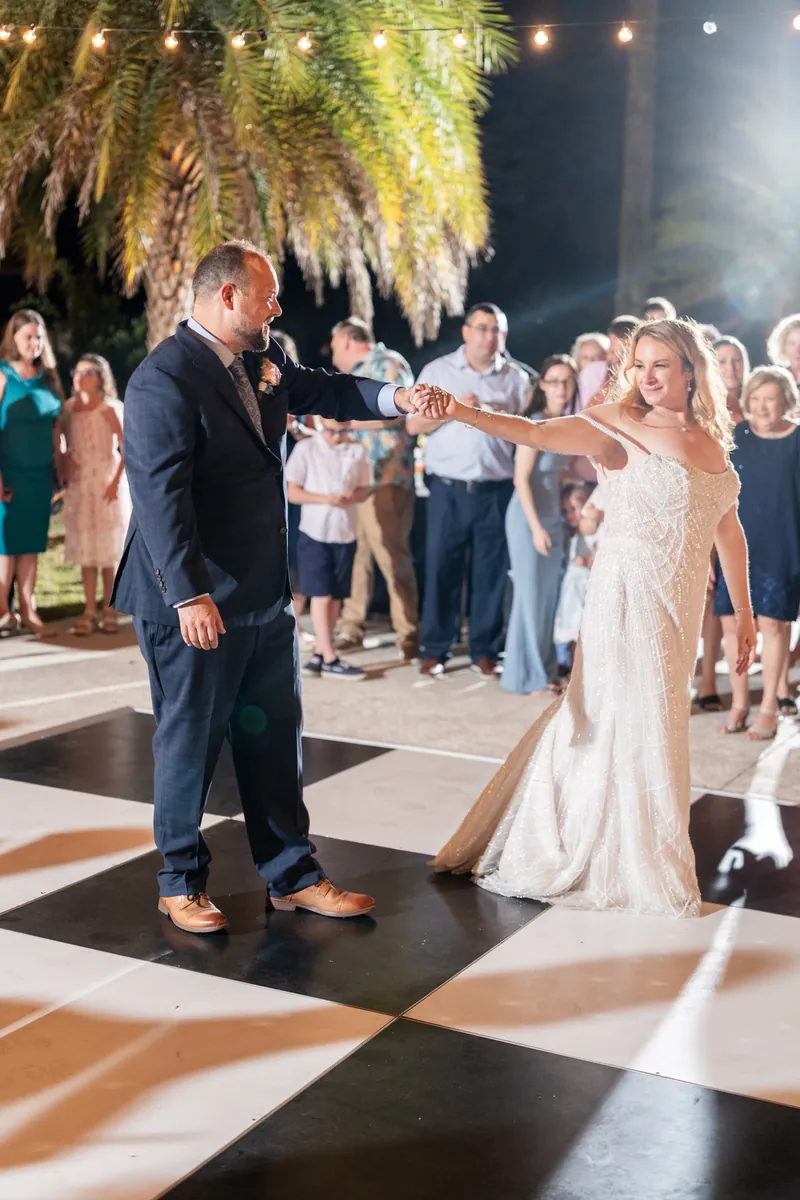 Von and Danielle dance together on an outdoor checkered floor beneath hanging greenery and string lights.