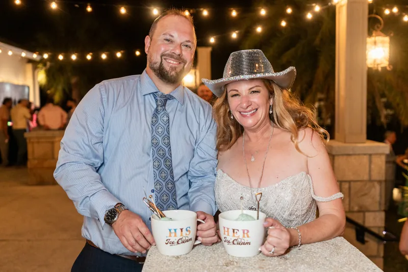 Von and Danielle hold personalized mugs while posing together under string lights, both smiling.