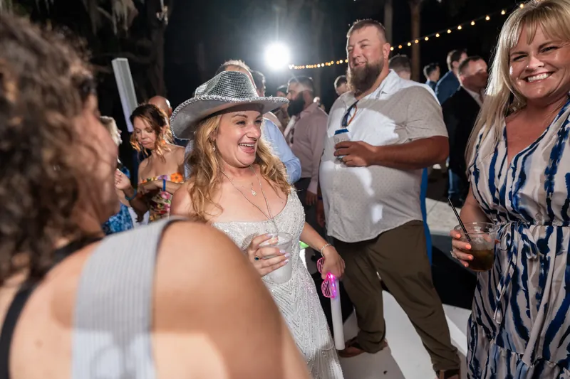 Danielle wears a cowboy hat and smiles while surrounded by guests during the nighttime reception.