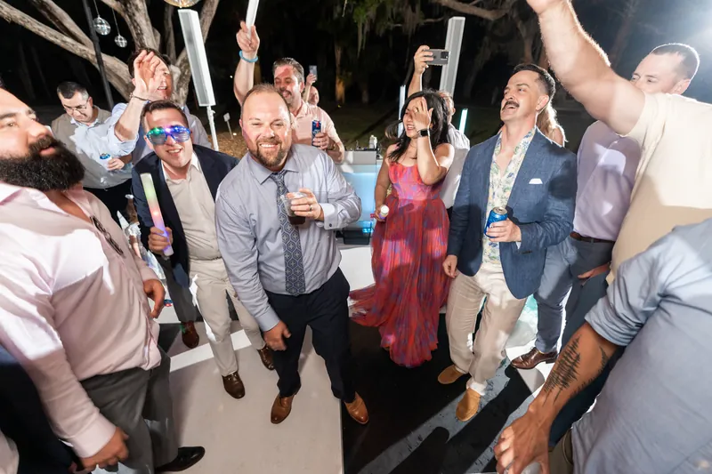 Wedding guests raise glasses and phones to toast Von and Danielle under string lights at their nighttime reception.