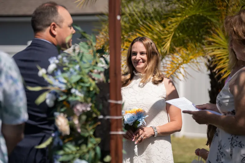A person in a white lace dress holds a small bouquet while smiling during an outdoor ceremony at the Airbnb in St. Augustine.