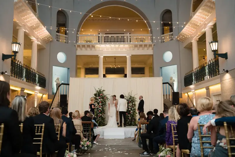 Wide ceremony shot showing Lightner Museum grand ballroom with string lights