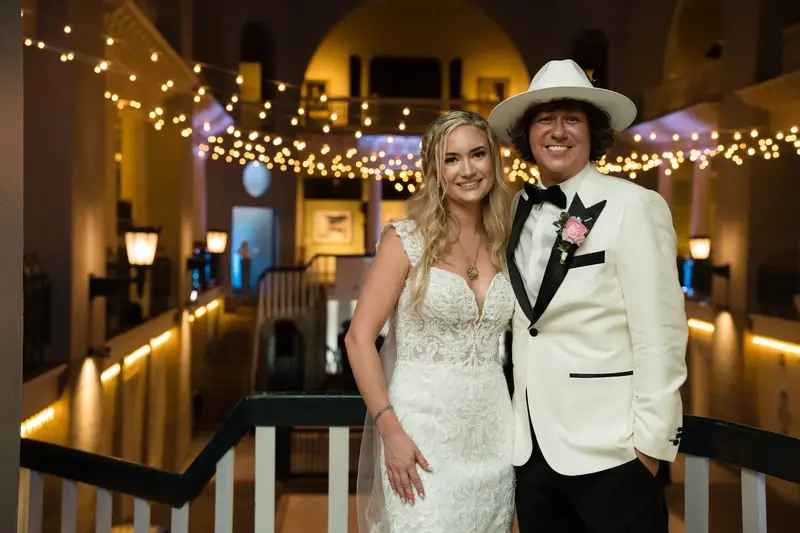 Couple portrait under string lights with groom wearing cowboy hat