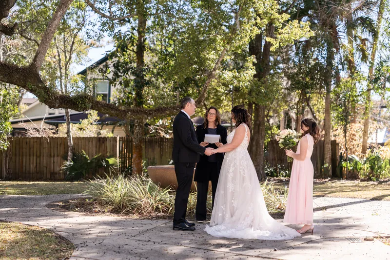 Wide view of the ceremony under oak trees with their daughter standing beside them