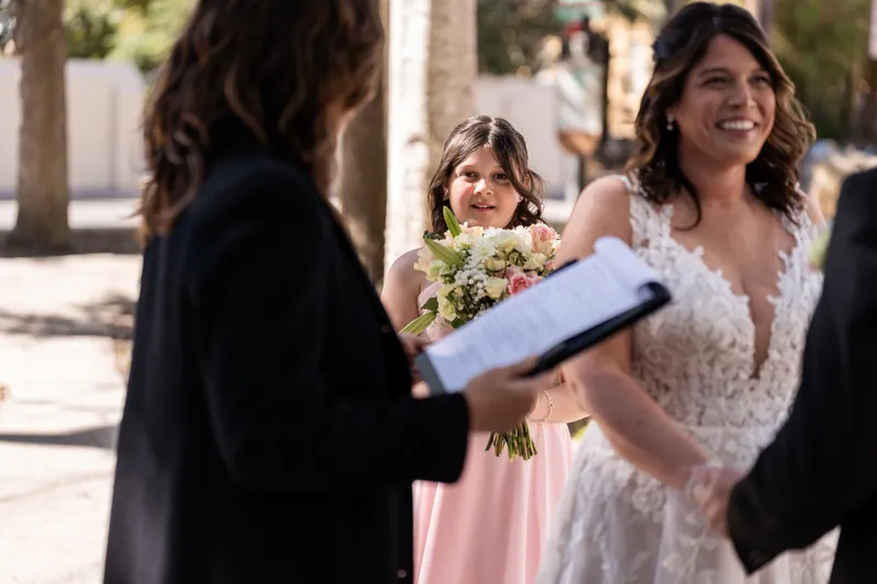Their daughter peeking around the officiant with Jennifer smiling beside her