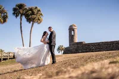 Bride and groom leaning together beneath palm trees at Castillo de San Marcos