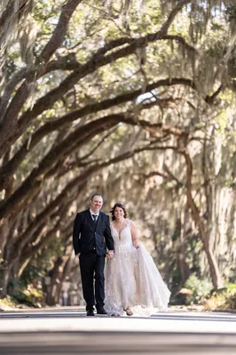 Newlywed couple walking hand-in-hand under the Magnolia Street oak canopy