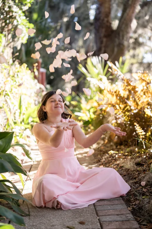 Their daughter tossing rose petals in a garden with warm backlight