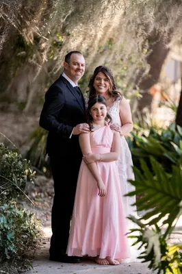 Jennifer in a white gown and Donnie in a dark suit stand together with the stone fortress tower and palms behind them.