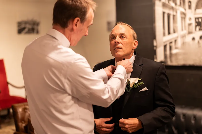 Groomsman adjusting groom's tie and calla lily boutonniere