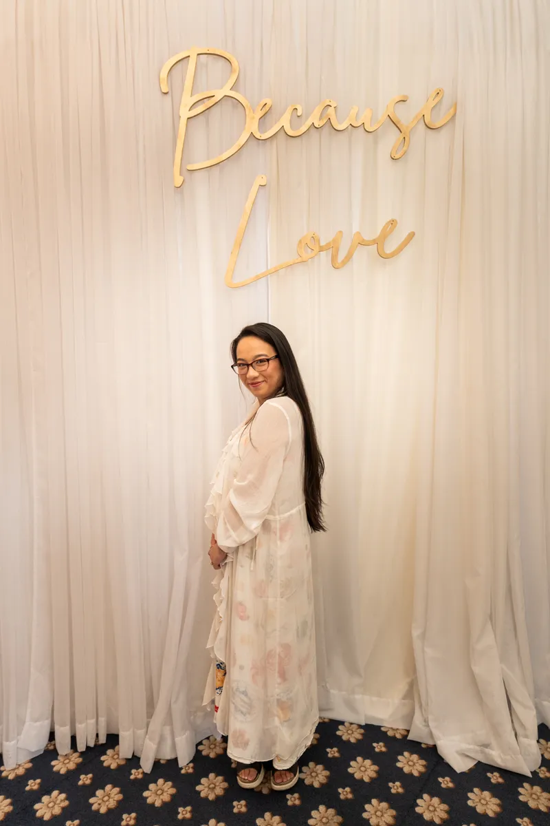 Bride posing in front of gold Because Love sign in her getting-ready robe