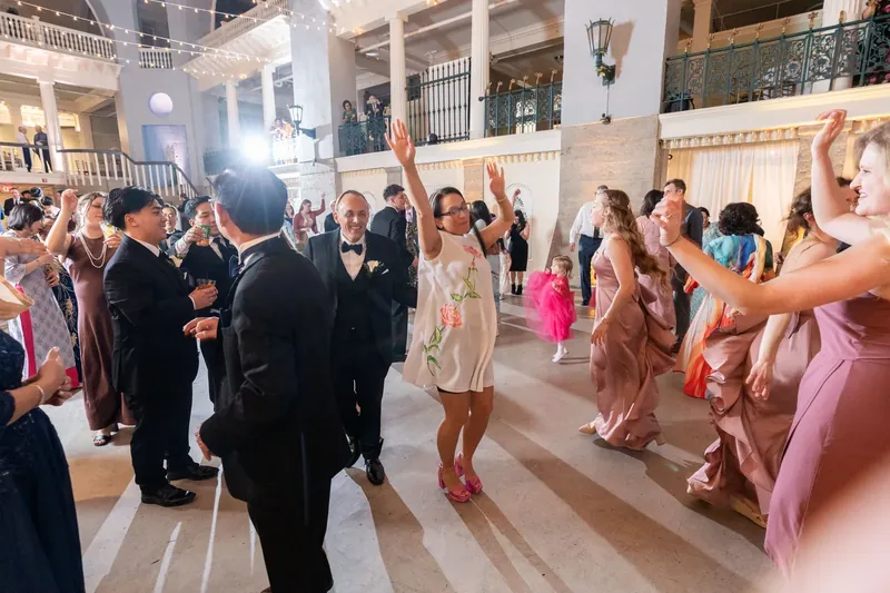 Guests dance and celebrate in the expansive ballroom at Lightner Museum, with men in tuxedos and women in various pastel