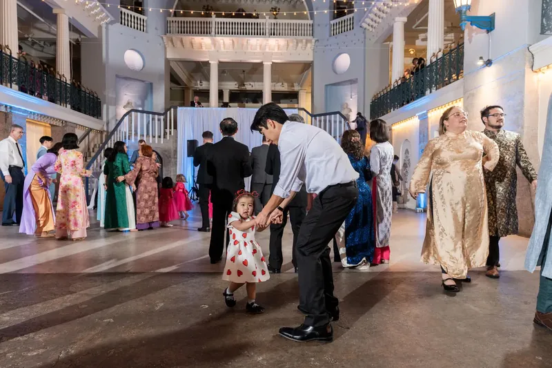A man dances with a young child in a floral dress as other guests gather around them in the museum's soaring atrium.
