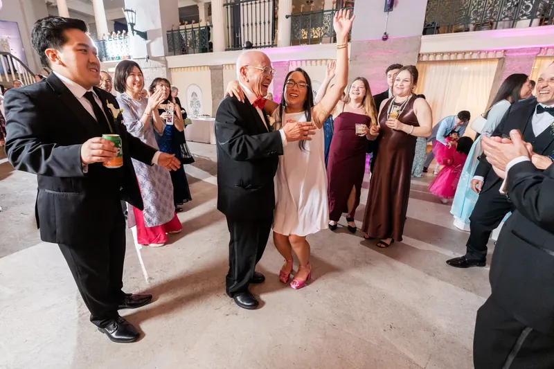 Two men dance while women in formal dresses clap and cheer during the celebration at Lightner Museum.