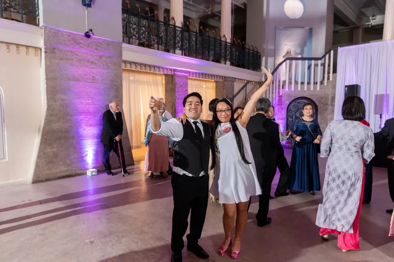 Jason and Elizabeth walk across the dance floor while guests socialize beneath the museum's illuminated gallery railings.