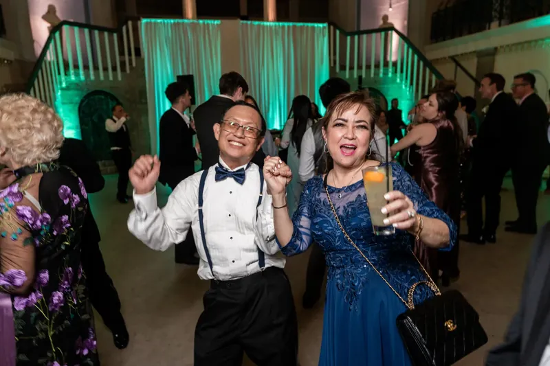 Guests dance with raised fists under turquoise uplighting at Lightner Museum's grand interior.