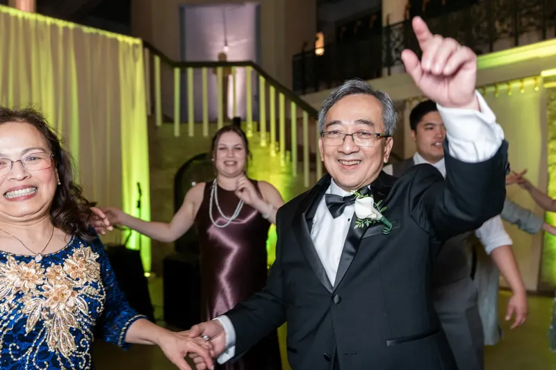 A man in a tuxedo raises his fist triumphantly while dancing at the reception.