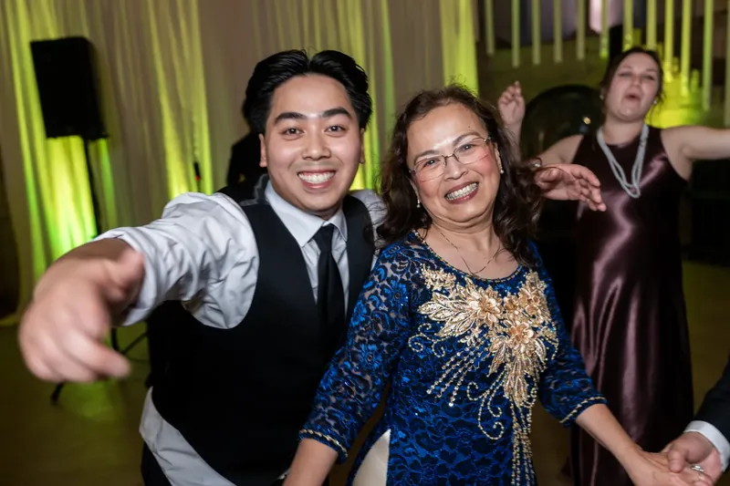 A young man in a vest and tie dances beside a woman in a sequined blue dress.