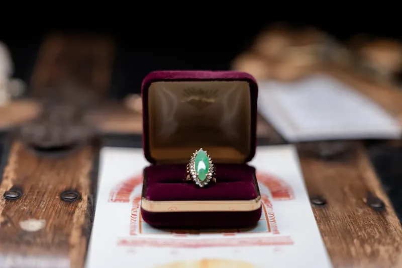 Emerald engagement ring nestled in burgundy velvet box on wooden table at Lightner Museum.