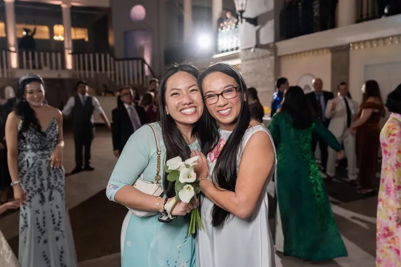 Two women hold bouquet and smile together during evening reception at Lightner Museum.