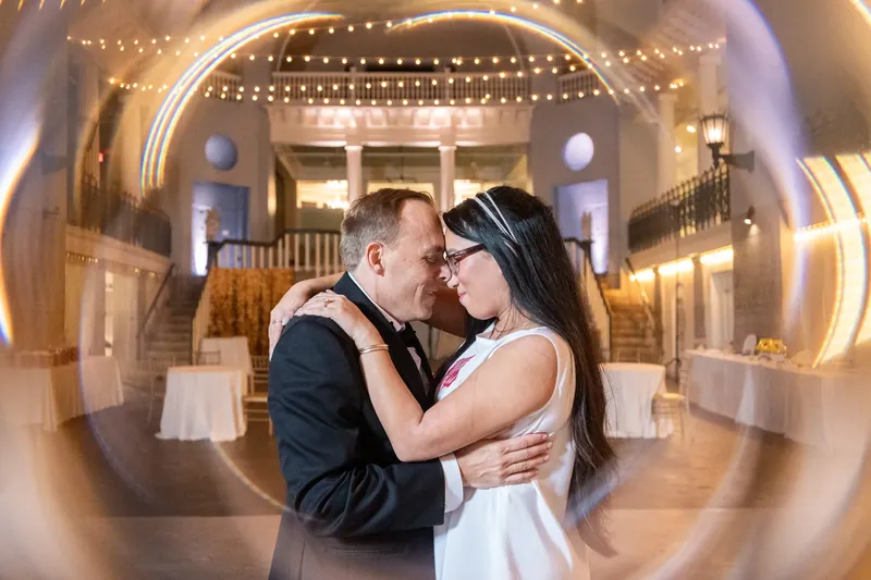 Jason kisses Elizabeth in a circular lens effect as the lit ballroom and grand staircase blur behind them.