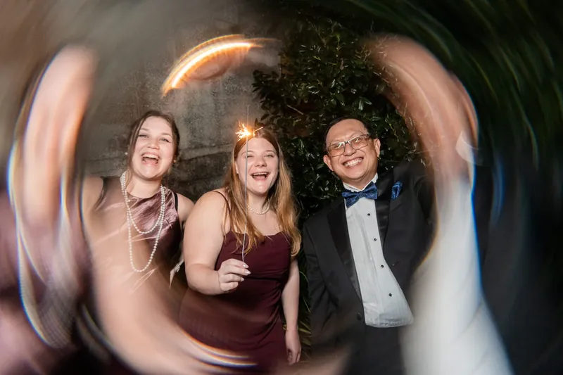 Three guests grin and gesture playfully through a circular lens capturing the celebration at the Lightner Museum.