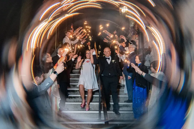 Elizabeth and Jason lead guests down an illuminated staircase framed through a distorted circular lens at the venue.
