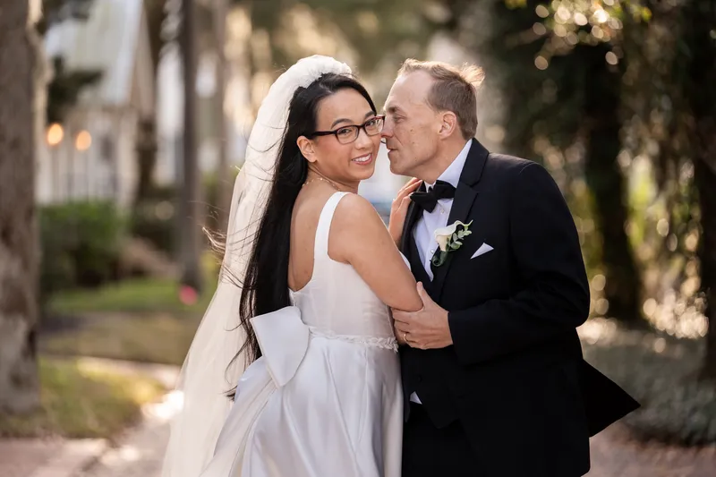 Close-up of bride and groom nose-to-nose on a tree-lined path in golden afternoon light