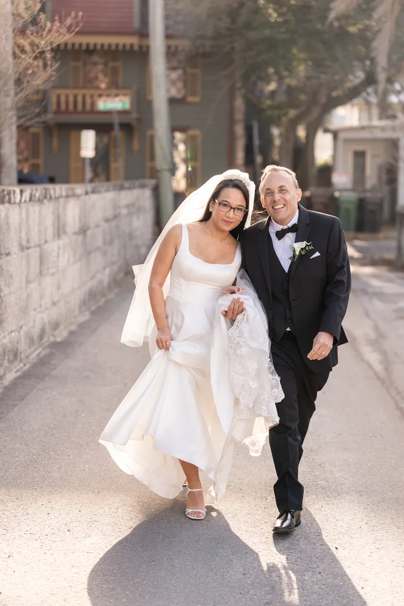 Bride and groom walking down a St. Augustine side street, bride holding up her lace train