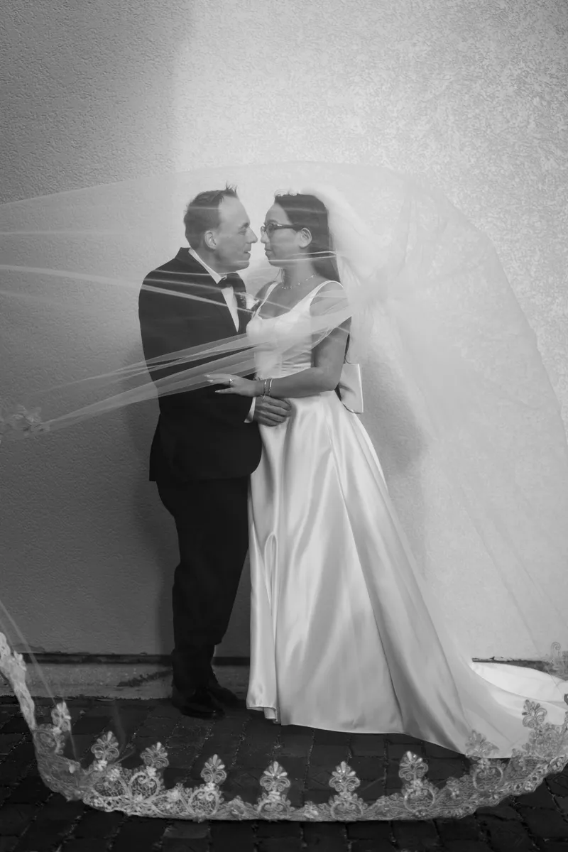 Black and white portrait of couple beneath the cathedral-length veil with lace detail