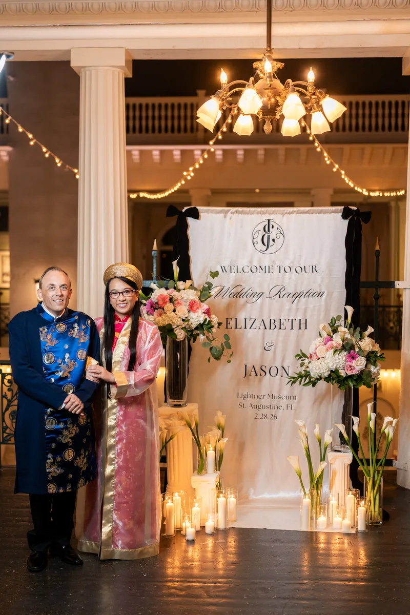 Elizabeth and Jason in Vietnamese ao dai at the welcome sign with candles and flowers at Lightner Museum