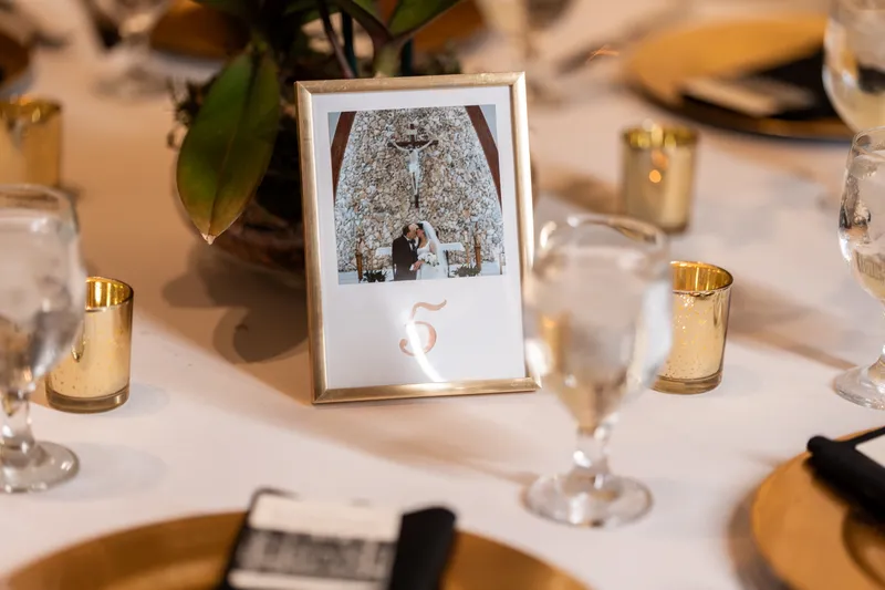 Table number in gold frame with couple's photo, gold charger and black napkin
