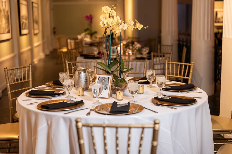 Reception tablescape with white orchid centerpiece, gold chargers, and chiavari chairs at the Lightner Museum
